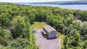 A two-story house with a large front yard, surrounded by dense forest and a lake in the background. - Spacious Home Sleeps 20! Dogs OK (Lansing)
