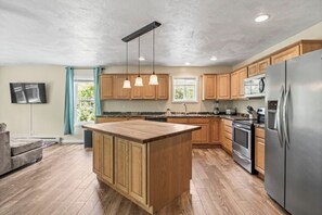 Cozinha moderna com armários de madeira, eletrodomésticos de aço inoxidável e iluminação pendente.