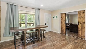 A kitchen with a wooden table, bar stools, and a window with curtains. - Spacious Home Sleeps 20! Dogs OK (Lansing)
