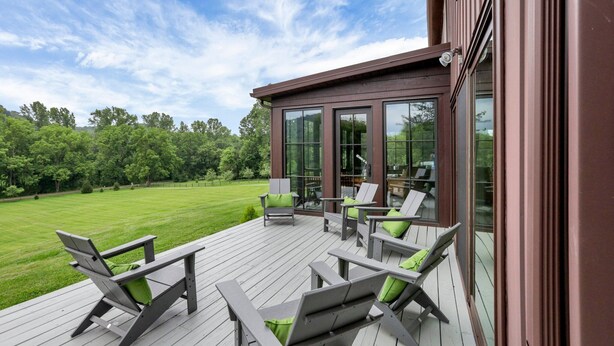 A deck with outdoor furniture and a glass door leading to a patio area. - Hillside haven on expansive grounds, heated pool, firepit, bocce court and more! (Logan)