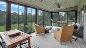 A sunroom with large windows, wicker furniture, a telescope, and a wooden table. - Hillside haven on expansive grounds, heated pool, firepit, bocce court and more! (Logan)