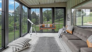 A spacious room with large windows, a comfortable sofa, a telescope, and a swing chair. - Hillside haven on expansive grounds, heated pool, firepit, bocce court and more! (Logan)