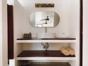 A bathroom with a white sink, a mirror with a gold frame, a ceiling fan, and a towel rack with towels. - El Ranchito Surfcamp (Guanico Abajo)