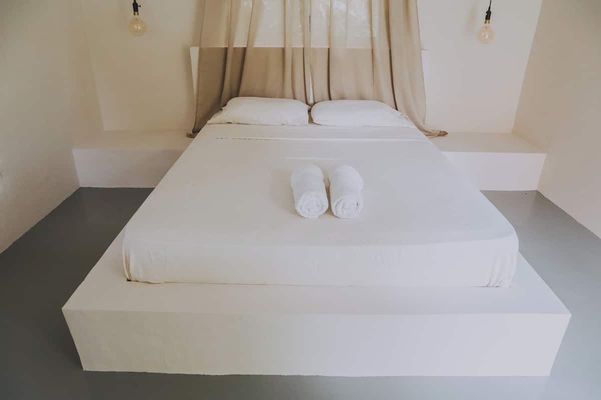 Uma cama bem arrumada com lençóis brancos e duas toalhas enroladas colocadas aos pés da cama.