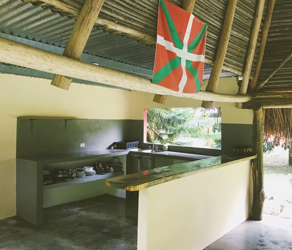 A kitchen with a large island, a sink, and a window overlooking greenery. - El Ranchito Surfcamp (Guanico Abajo)