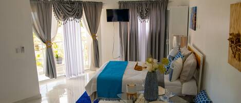 A hotel room with a bed, a TV, a table with a vase, and a sofa.