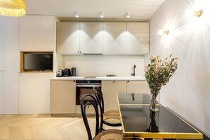 Uma cozinha moderna com armários brancos, forno embutido e uma área de refeições com mesa e cadeiras pretas.