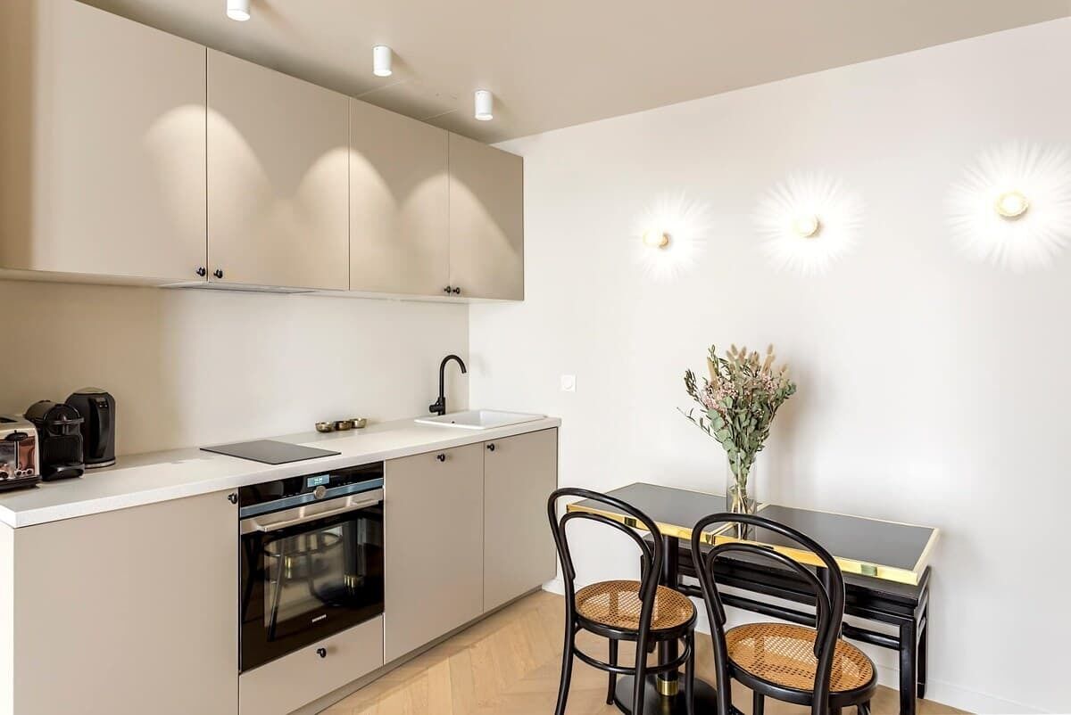 A modern kitchen with white cabinets, a black countertop, and a dining area with a table and chairs.