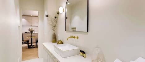 Un baño moderno con un tocador blanco, un espejo grande y un tarro de vidrio.
