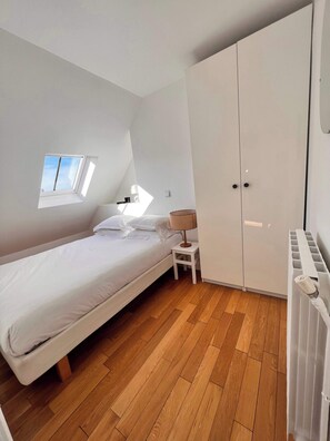 Quarto com cama, mesa de cabeceira, luminária, guarda-roupa e claraboia.