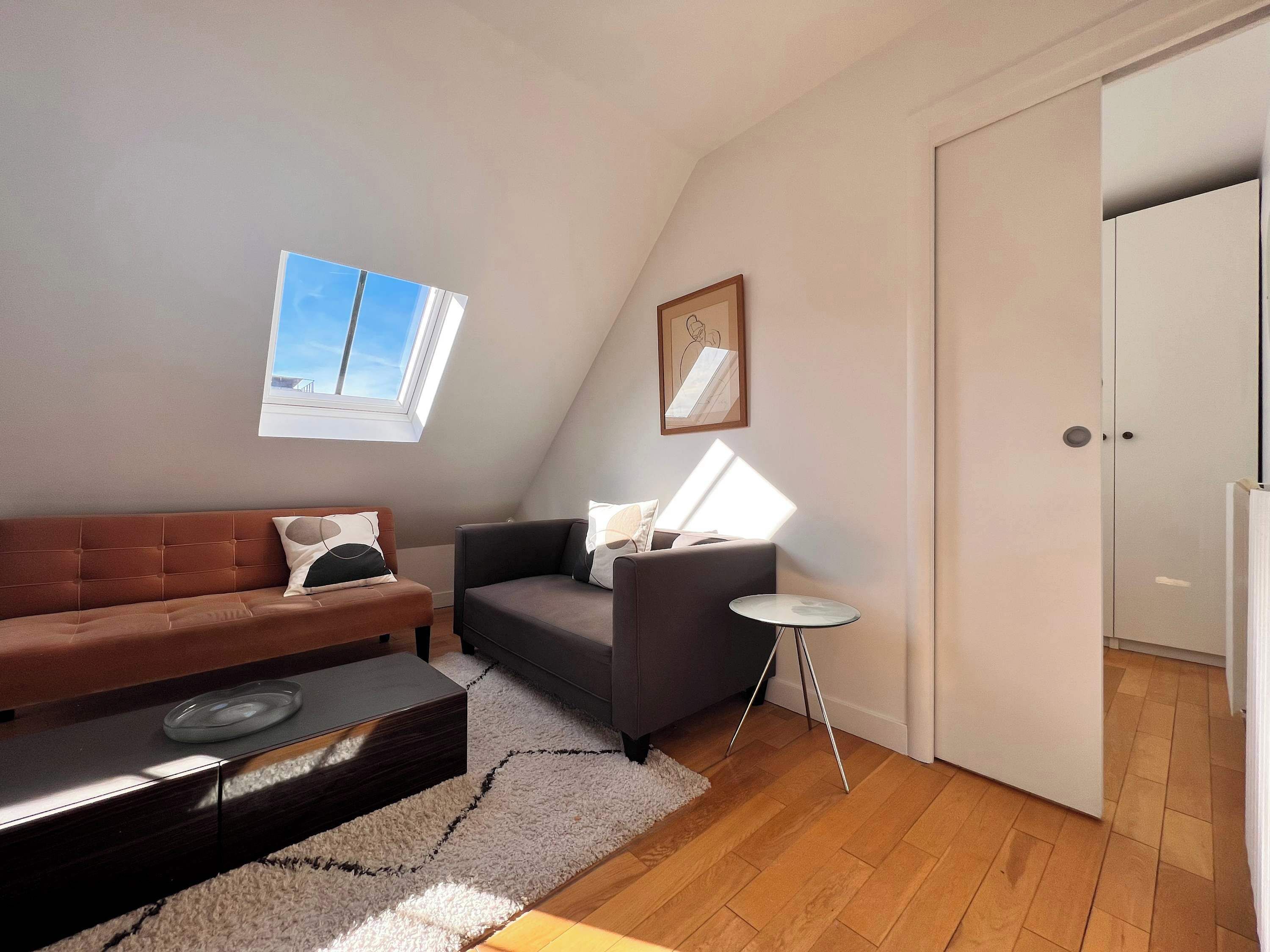 A loft-style room with a brown sofa, a gray armchair, a small round table, and a white door.