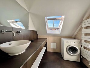 Um banheiro moderno com uma cuba grande, máquina de lavar embutida e um skylight.