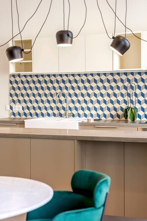 Una cocina moderna con un salpicadero geométrico, encimera blanca y una silla verde.