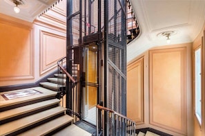 Uma escadaria imponente com corrimão de metal preto e degraus bege, que leva a um espaço com uma janela grande e uma porta.