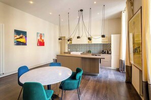 Una cocina moderna con una isla central, un comedor con una mesa redonda y sillas color turquesa, y obras de arte en las paredes.