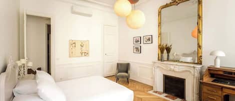 Un dormitorio con una cama grande, piso de madera, chimenea, espejo y escritorio.