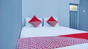 A bed with white bedding and red pillows, a red and white patterned throw blanket, and a blue door with a floral design. - Hotel O Sulthan Homestay Syariah 2 (Palembang)
