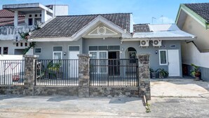 A two-story house with a tiled roof, a gated entrance, and a small front yard with potted plants. - Hotel O Sulthan Homestay Syariah 2 (Palembang)
