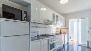 A modern kitchen with white cabinets, a built-in microwave, a stove, and a sink. - Estrela Azul 5AR (Caniço)
