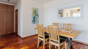 A dining area with a wooden table and chairs, a painting of a parrot, and a mirror on the wall. - Estrela Azul 5AR (Caniço)