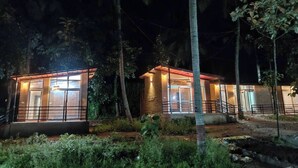 Two small, well-lit cabins surrounded by dense foliage at night. - Kabini Earthern Cottages Lakeside Farmstay
 (Holehundi)