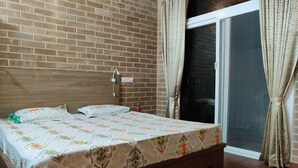 A bedroom with a wooden bed, a brick wall, a sliding glass door, and a curtain. - Kabini Earthern Cottages Lakeside Farmstay
 (Holehundi)