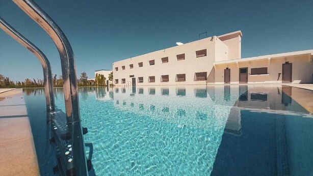 A swimming pool with a modern building in the background. - Hôtel Debrazza (Ouled Tayeb)