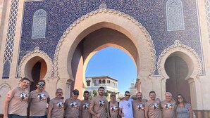 A group of people standing in front of a large archway with intricate blue and beige patterns.