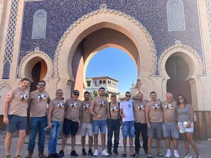 A group of people standing in front of a large archway with intricate blue and beige patterns.