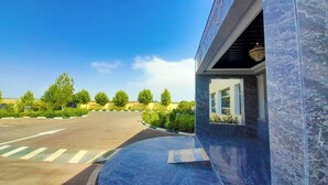 A parking lot with a clear sky, trees, and a building entrance with a window. - Hôtel Debrazza (Ouled Tayeb)