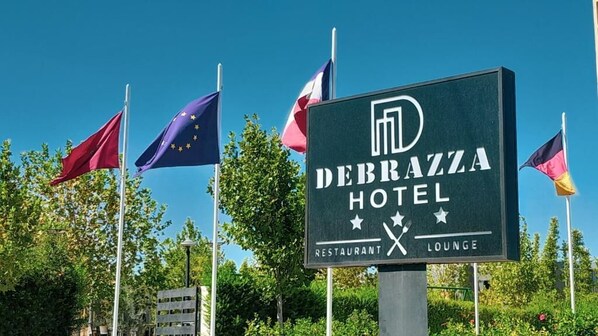 A sign for Debrazza Hotel with flags, a restaurant, and a lounge.
