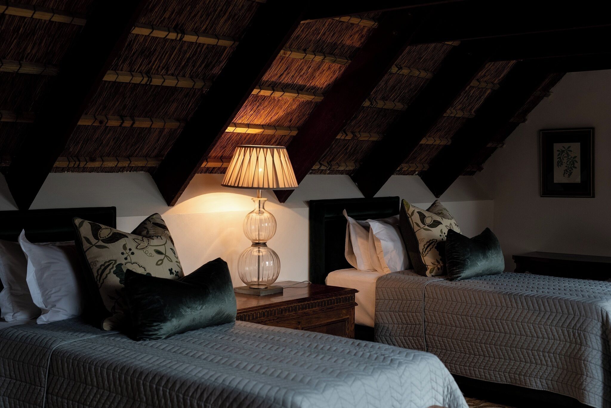 Une chambre avec deux lits, une table de chevet avec une lampe et un plafond recouvert de chaume.