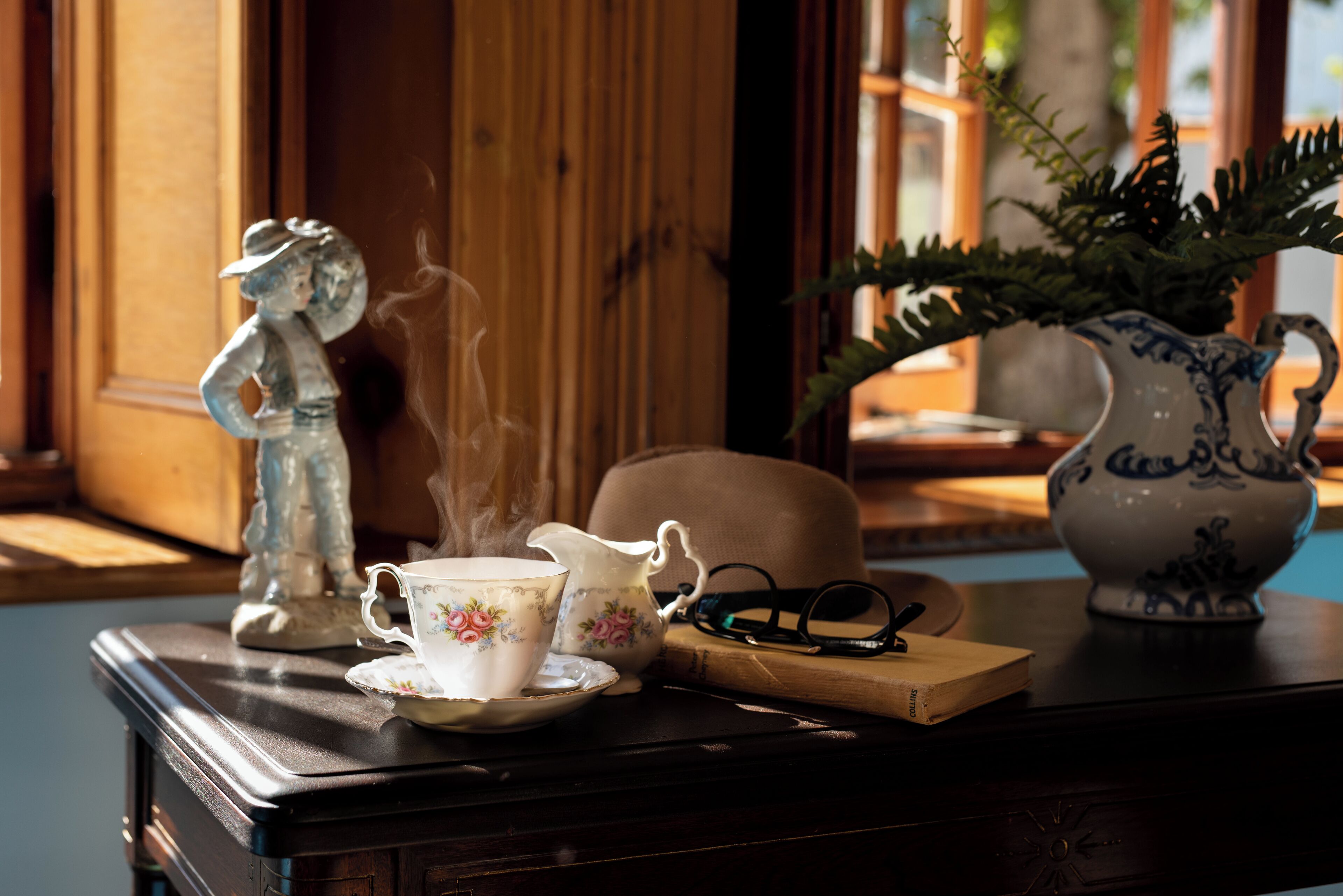 A wooden table with a teapot, teacup, saucer, and a figurine.