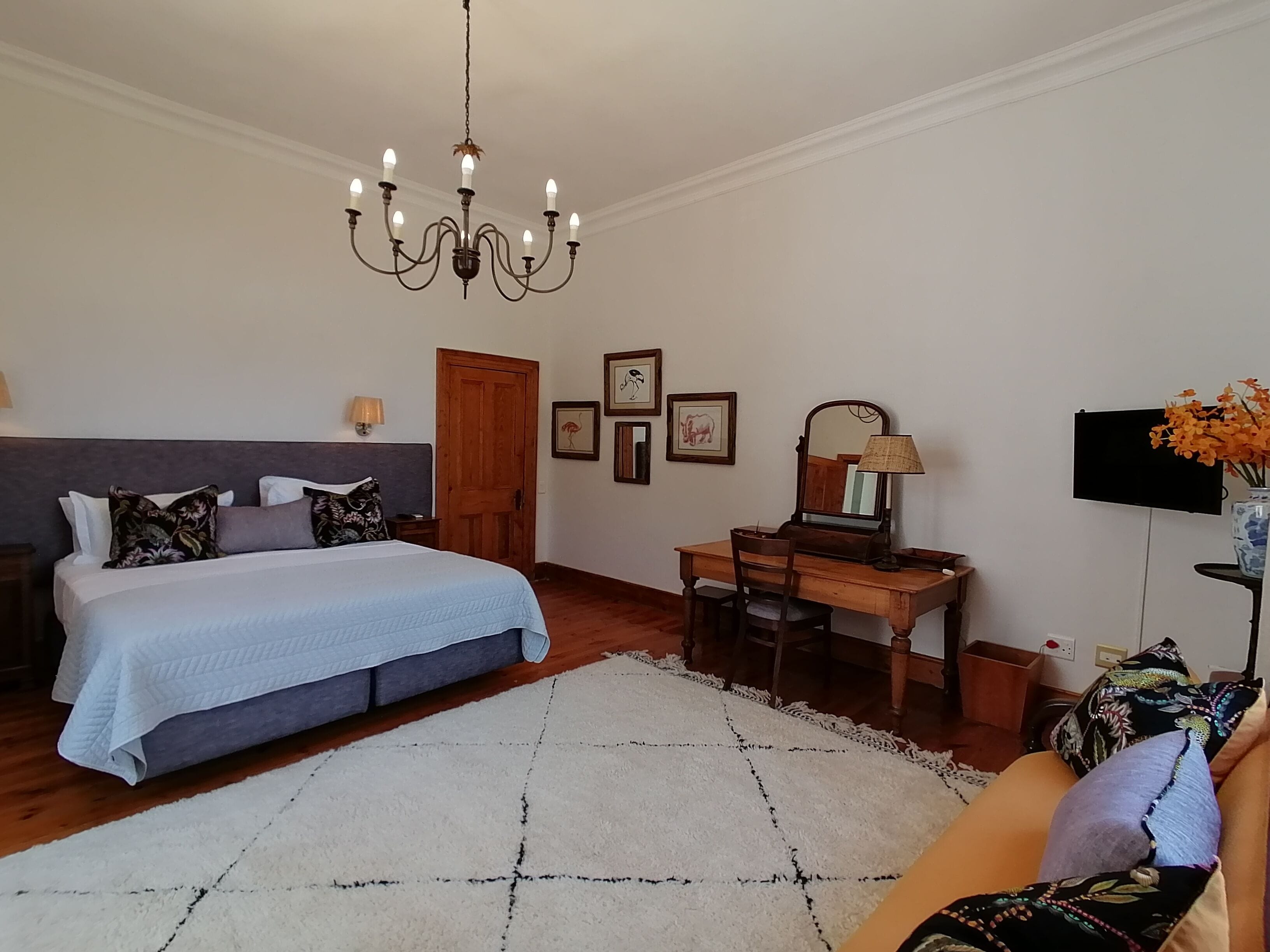 Een slaapkamer met een bed, een bureau, een stoel, een televisie en een kroonluchter.