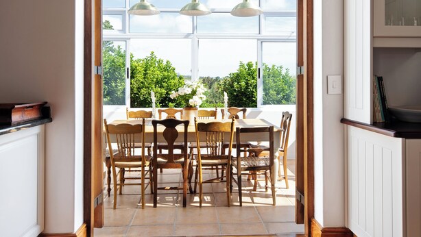 A kitchen with wooden flooring, a dining area with a table and chairs, and a view through a large window to the outdoors. - Avontuur Manor House (Stellenbosch)