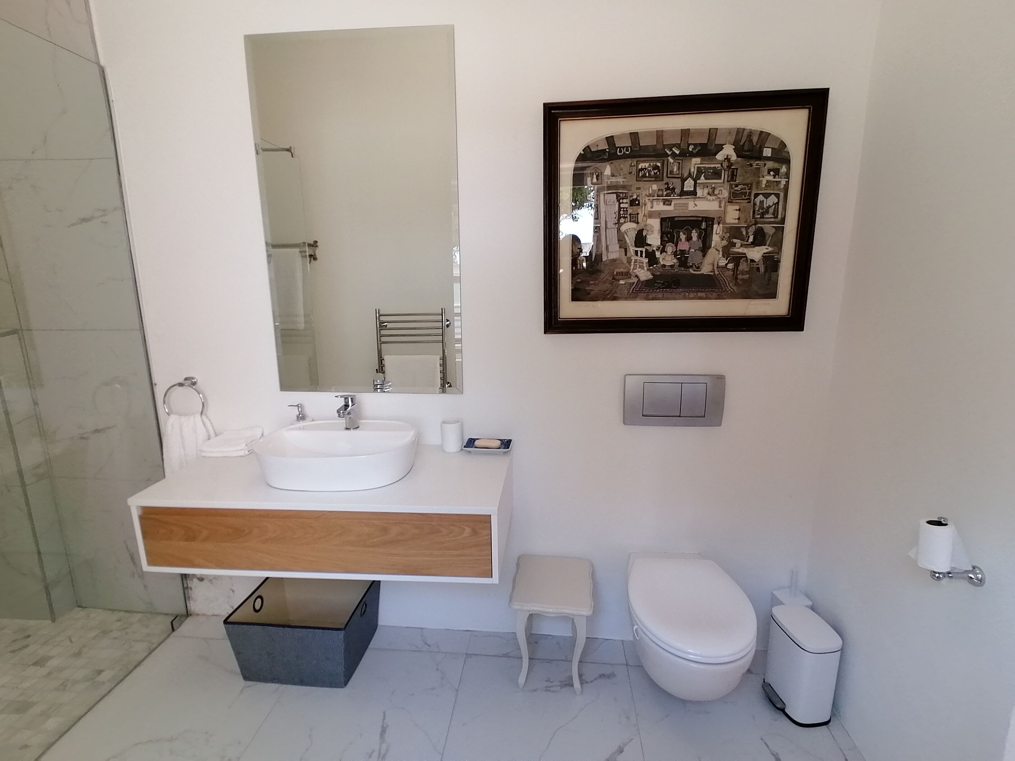 A modern bathroom with a large mirror, a sink, a toilet, and a framed picture on the wall.