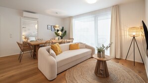 Una sala moderna con sofá, mesa de comedor, sillas, una mesita auxiliar con una planta y un ventanal con cortinas.