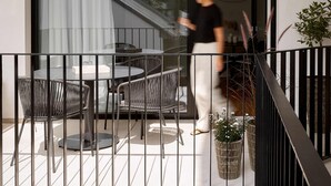 Un balcón moderno con puerta de vidrio, mobiliario de mimbre y plantas en macetas.