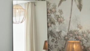 Un dormitorio con cama, lámpara de noche, espejo, pared con estampado floral y lámpara colgante.