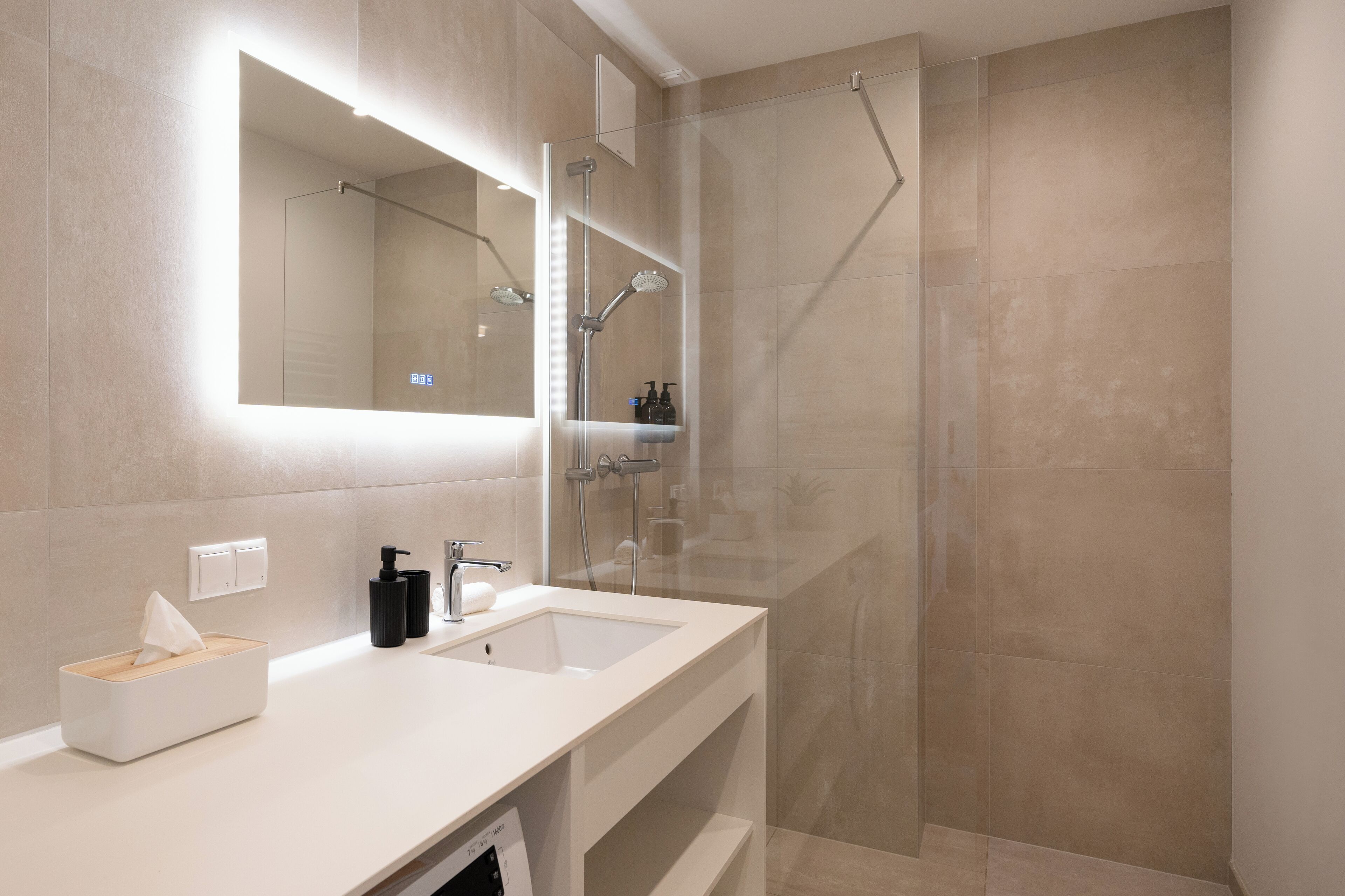 A modern bathroom with a large mirror, a sink, and a shower enclosure.