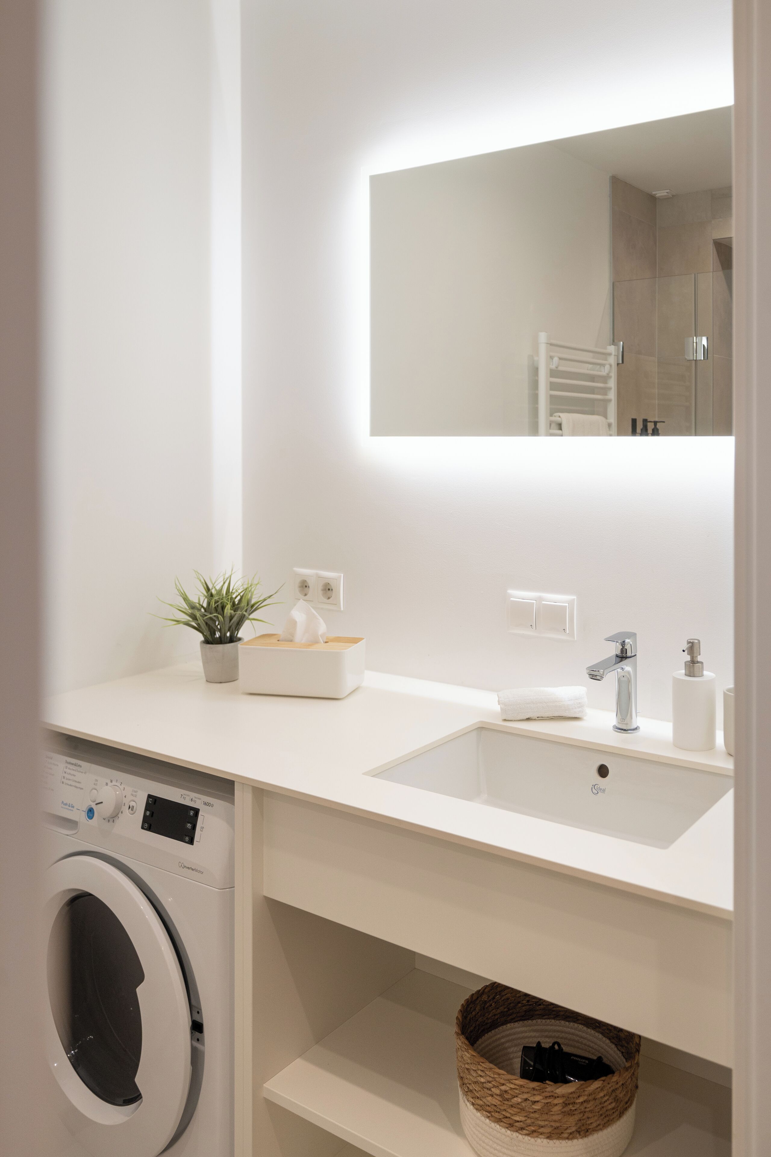 Ein modernes Badezimmer mit Waschbecken, Spiegel, Waschmaschine und Wäschekorb.