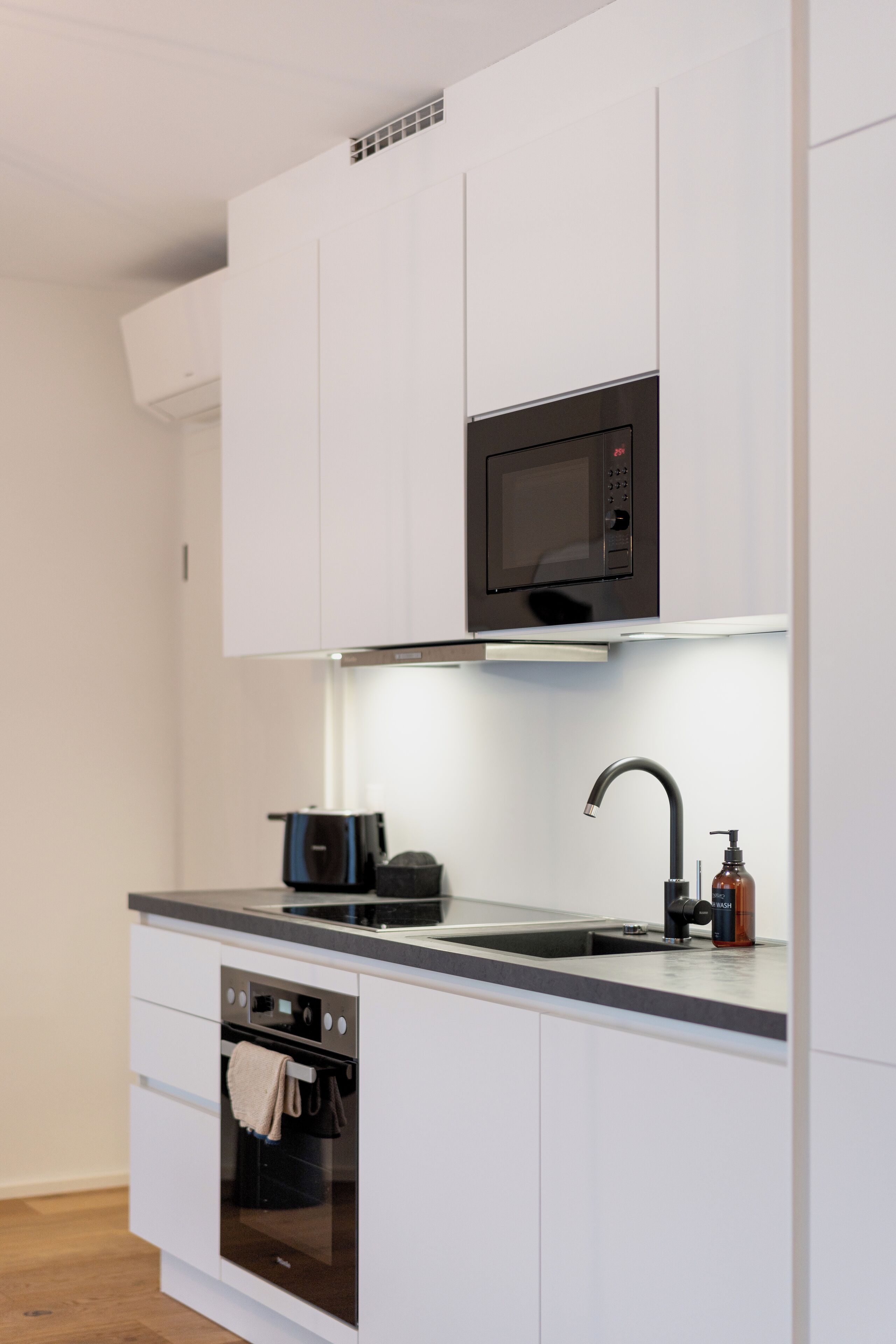 A modern kitchen with white cabinets, a built-in microwave, a stainless steel sink, and an oven.