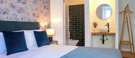 A bedroom with a bed, a nightstand, a lamp, a bathroom with a sink and mirror, and a wooden ladder.