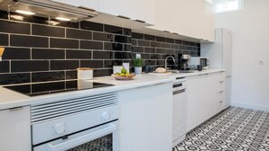 A modern kitchen with black and white tiles, a built-in stove, and a coffee maker. - Succeed Campo Pequeno Suites (Lisbon)