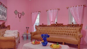 Un salón decorado en tonos rosas, con sofá, sillón y una mesa con fruta y un florero.