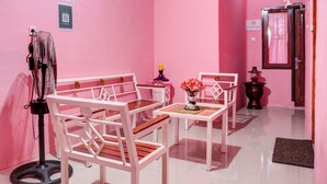 Una habitación decorada en tonos rosados, con muebles blancos, entre ellos una mesa y sillas, un pequeño florero decorativo y un ventilador.