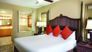 Une chambre d’hôtel avec un grand lit, une tête de lit en bois, une salle de bain avec baignoire et un ventilateur de plafond.