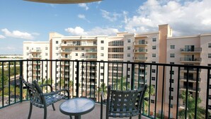 Un balcon avec deux chaises et une table, donnant sur un immeuble résidentiel à plusieurs étages, lui aussi doté de balcons.
