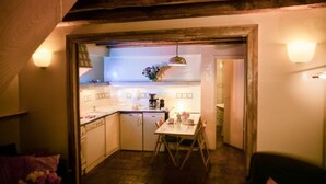 Une cuisine chaleureuse avec une table à manger, des poutres en bois et une vue sur la pièce adjacente.