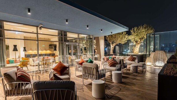 Un área de estar moderna al aire libre con mobiliario contemporáneo y una pared de vidrio con vistas a la ciudad.
